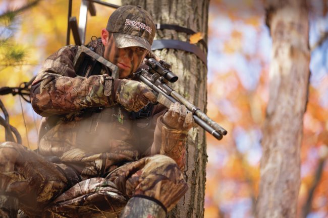 Air rifle hunter in tree stand aiming at prey below.