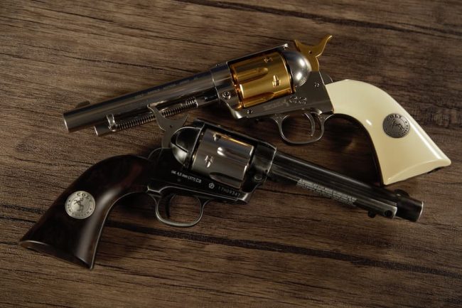 historical replicas. two colt single action army revolvers on a wood table.